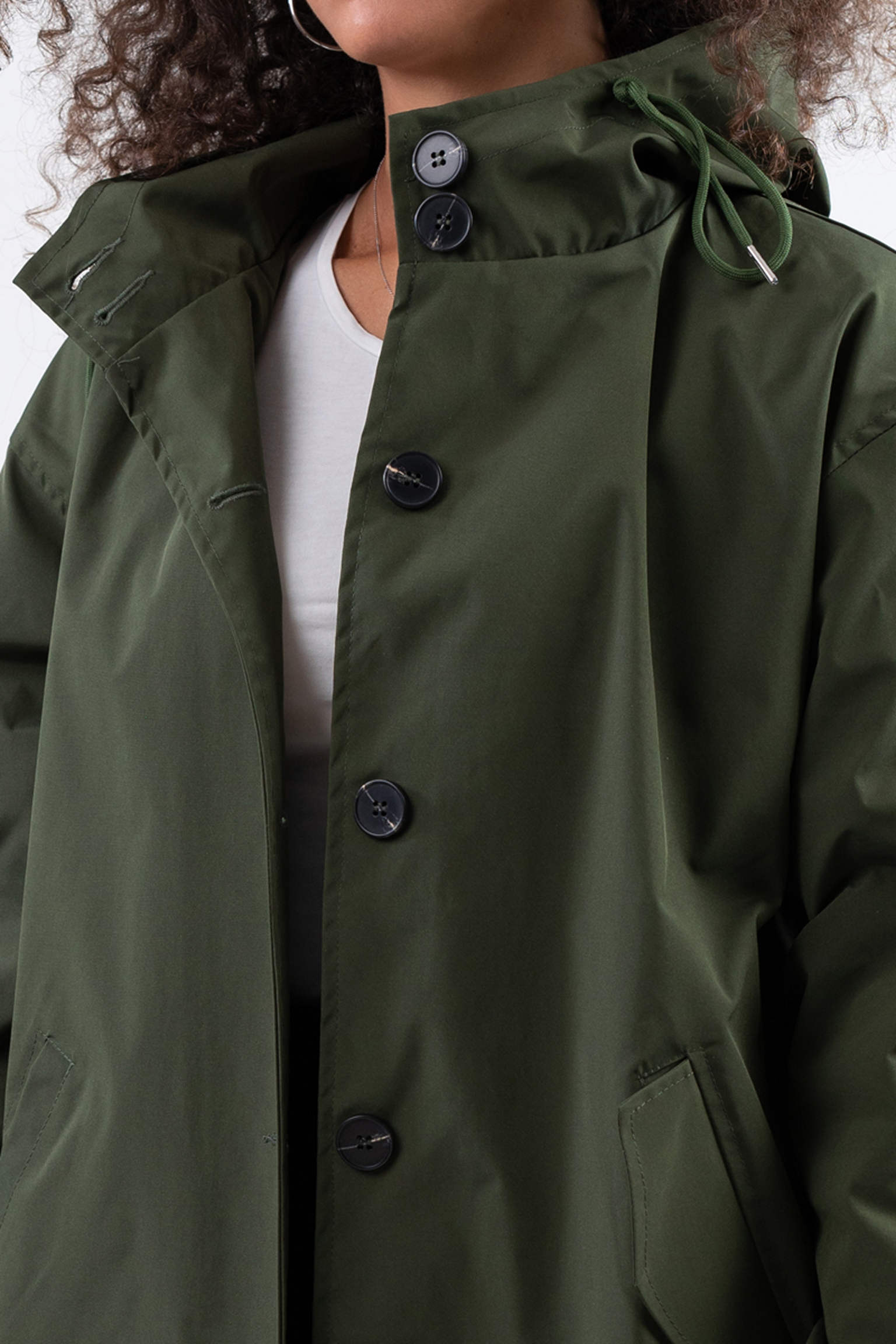 A person wears the Icon Windbreaker Rain Jacket—an olive green hooded coat with large black buttons and pockets—partially buttoned over a white shirt. The person's face is not visible.