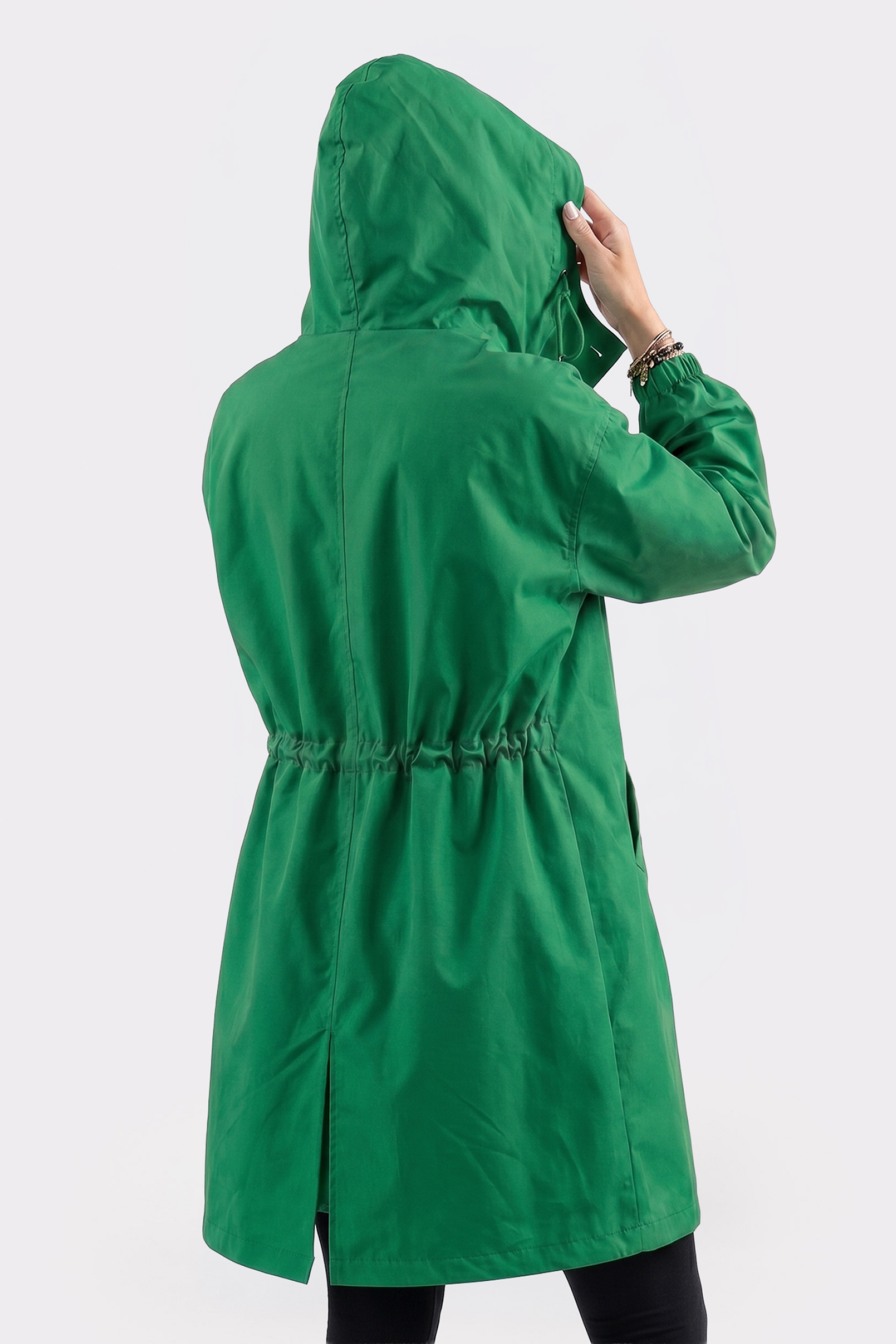 A person wearing the Icon Windbreaker Rain Jacket in bright green stands facing away from the camera, holding the hood's edge. The jacket features an elastic waistband and side pockets, set against a plain white background.