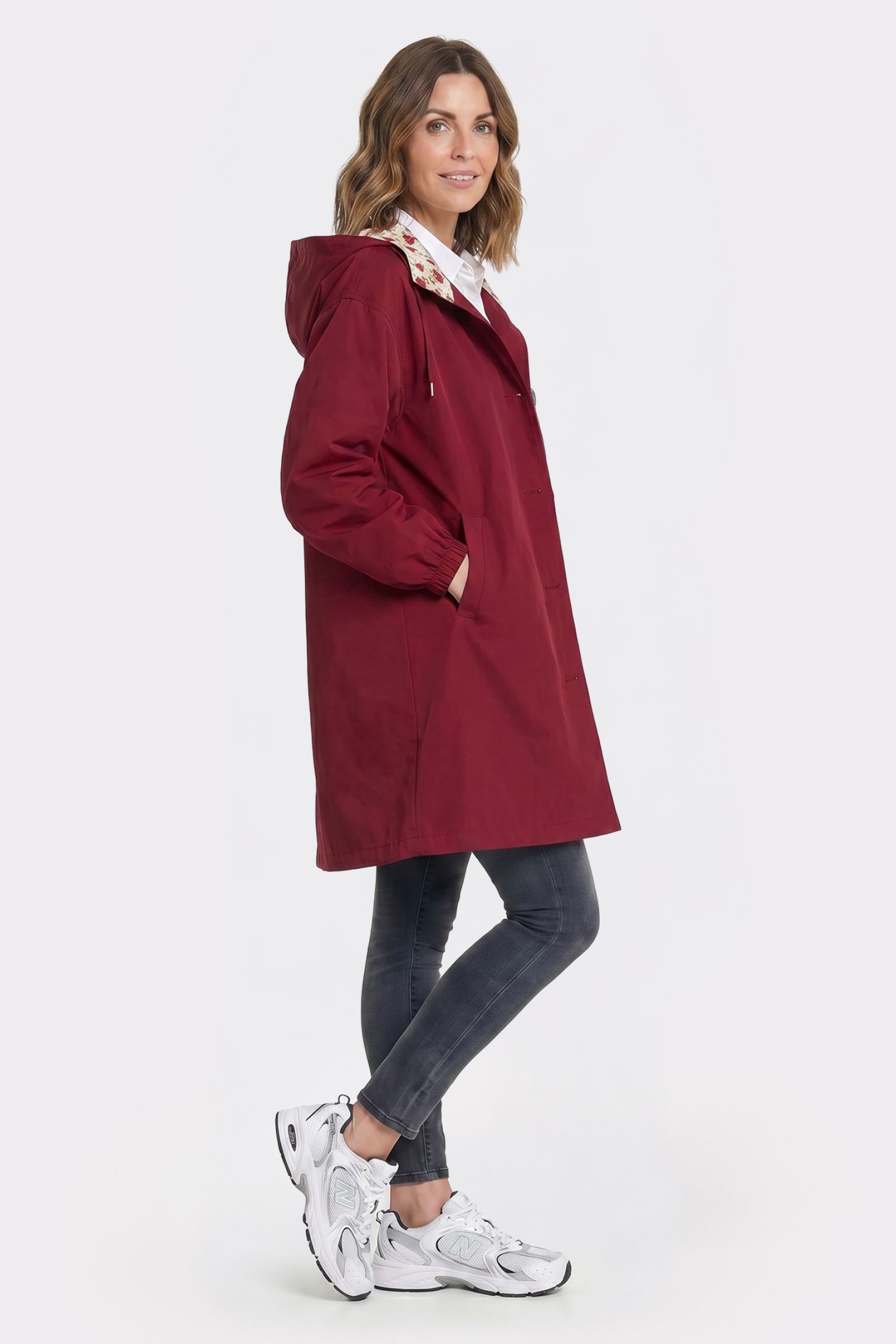 A woman stands in profile against a plain white background, wearing the Icon Windbreaker Rain Jacket with dark skinny jeans and white sneakers.