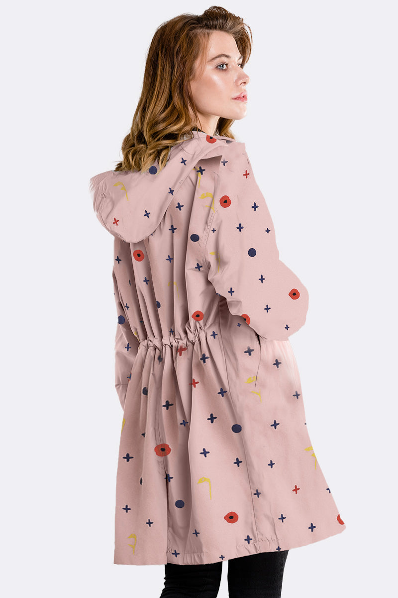 A person with wavy, shoulder-length hair faces away, wearing the looselyboho DOT & BLOOM WINDBREAKER—a light pink, water-resistant jacket with an elastic waist and colorful geometric patterns—set against a plain light gray background.