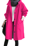 A person is wearing a bright pink long coat with black buttons from the iconic BARBARA PINK WINDBREAKER OUTFIT by looselyboho. They have their hands in the coat pockets and are also wearing a dark gray scarf, white shirt, and black pants. The person is carrying a black bag.