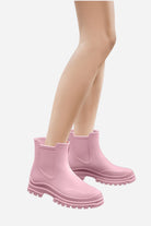 A person wearing pink Non-Slip Rain Boots from looselyboho stands on a plain white background. The boots have a chunky sole, SuperGrip Soles, and a pull-on style with no visible laces. The image focuses on the legs and feet, revealing smooth skin.