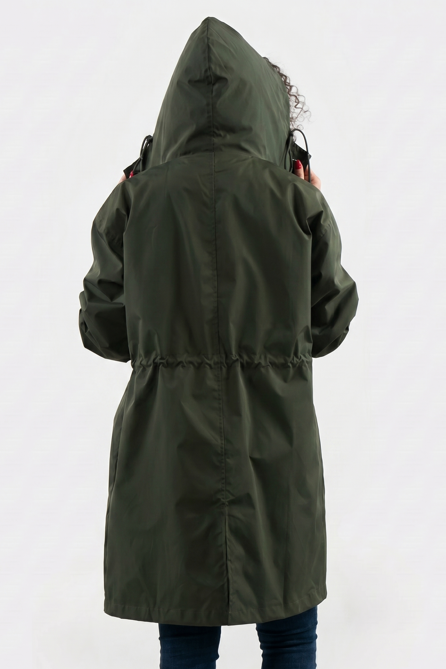 A person wearing The Water Resistant Hooded Oversized Windbreaker Rain Jacket in olive green is shown from the back, adjusting the hood. The hip-length jacket features a cinched waist against a plain white background.