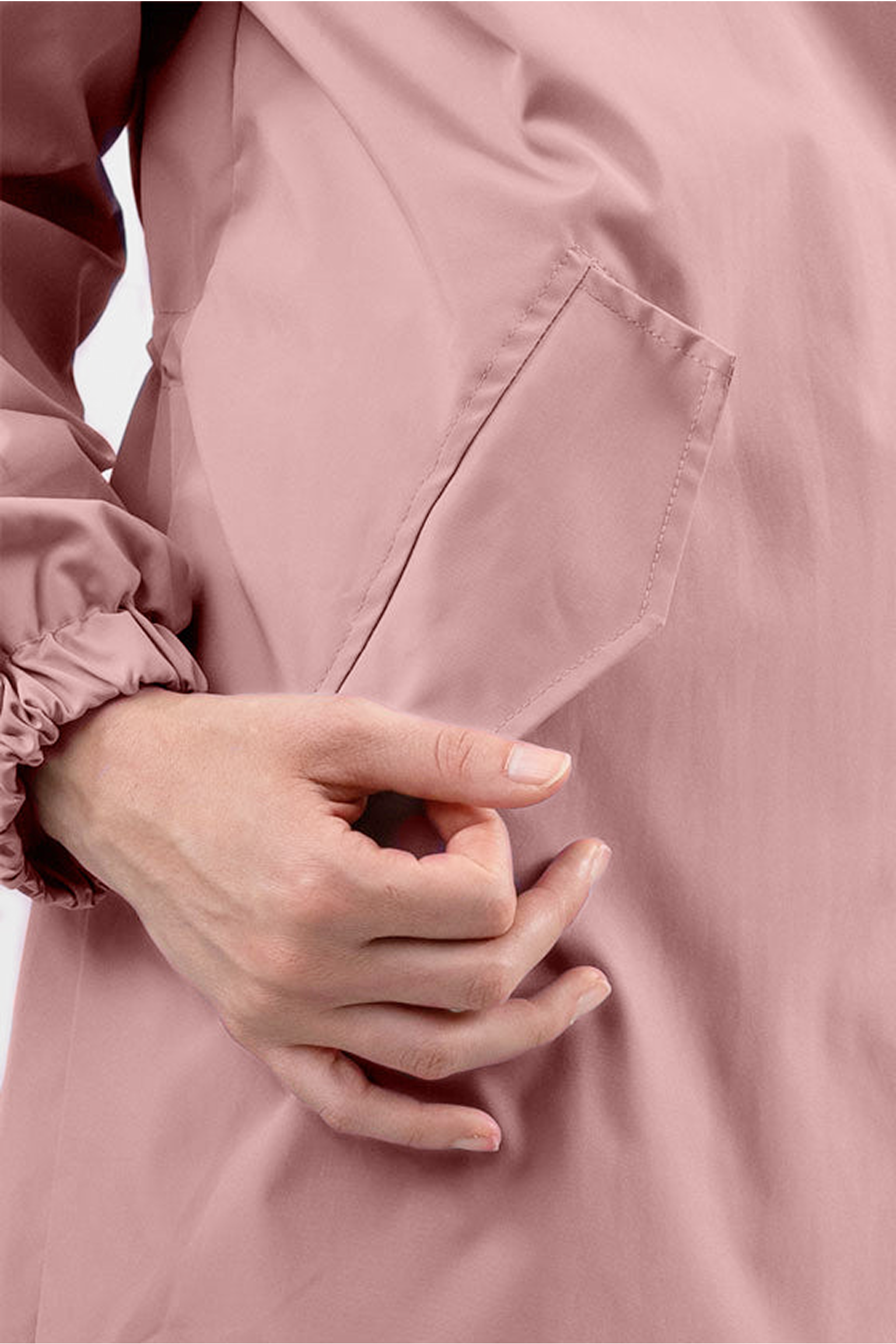 A hand is shown slipping fingers into the angled pocket of the light pink Icon Windbreaker Rain Jacket, which features an elastic cuff. The plain, light background highlights the jacket's details.