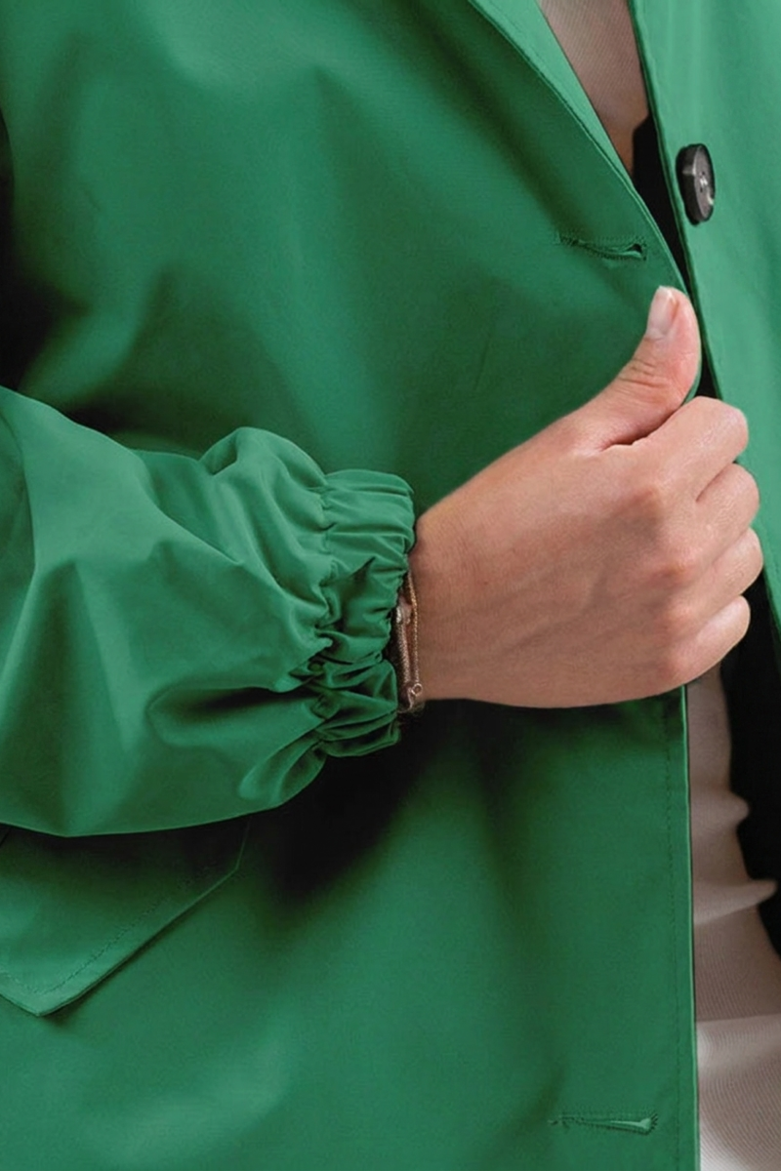 Someone gives a thumbs up while wearing the Icon Windbreaker Rain Jacket, identifiable by its green color and elastic cuffs. Only their hand, part of the arm, and the jacket are visible.