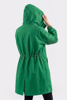 A person wearing the Icon Windbreaker Rain Jacket in bright green stands facing away from the camera, holding the hood's edge. The jacket features an elastic waistband and side pockets, set against a plain white background.
