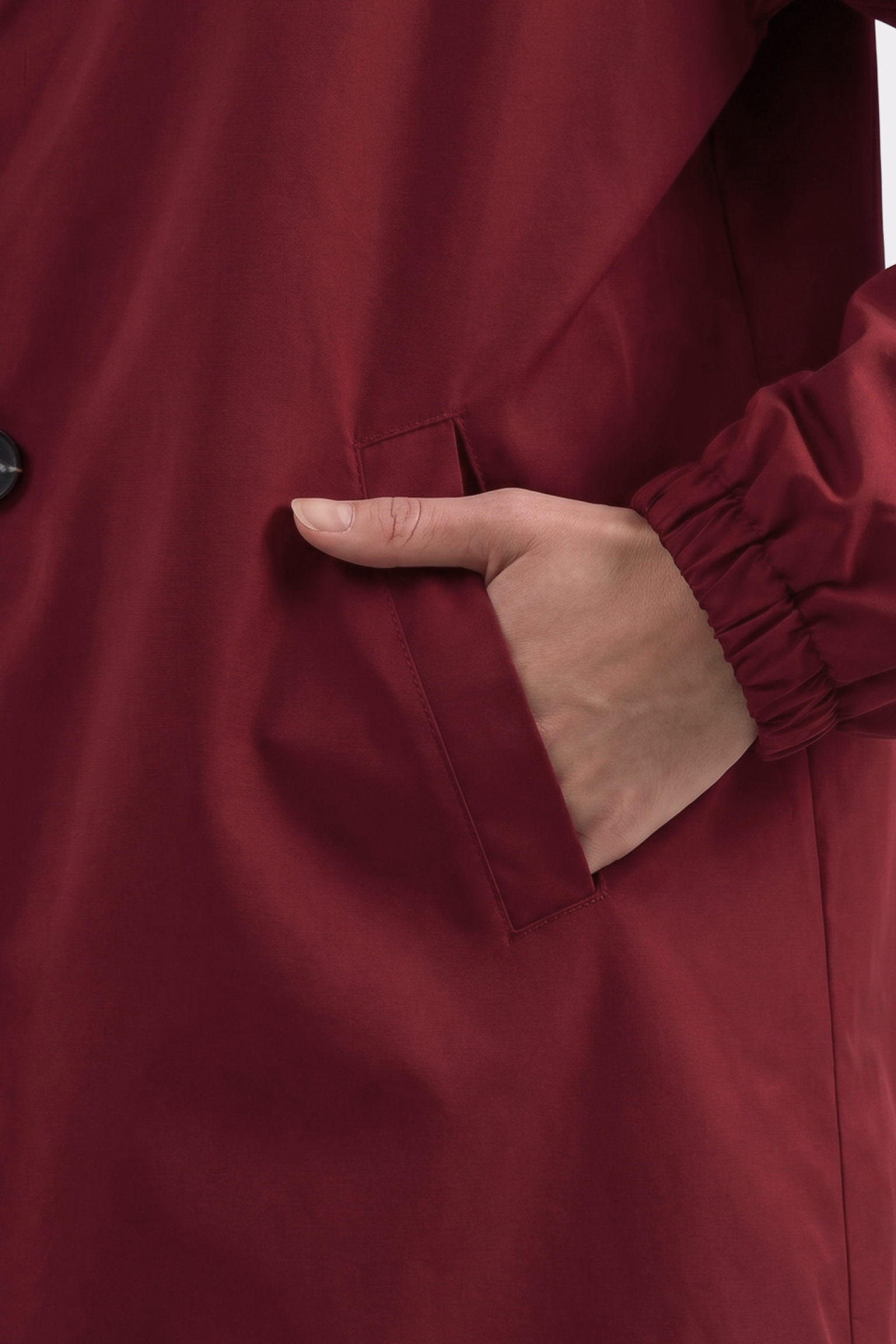 Someone is wearing The Water Resistant Hooded Oversized Windbreaker Rain Jacket in burgundy, with their right hand in the pocket. Only part of their arm and torso are shown. The jacket features an elastic cuff and button detail.