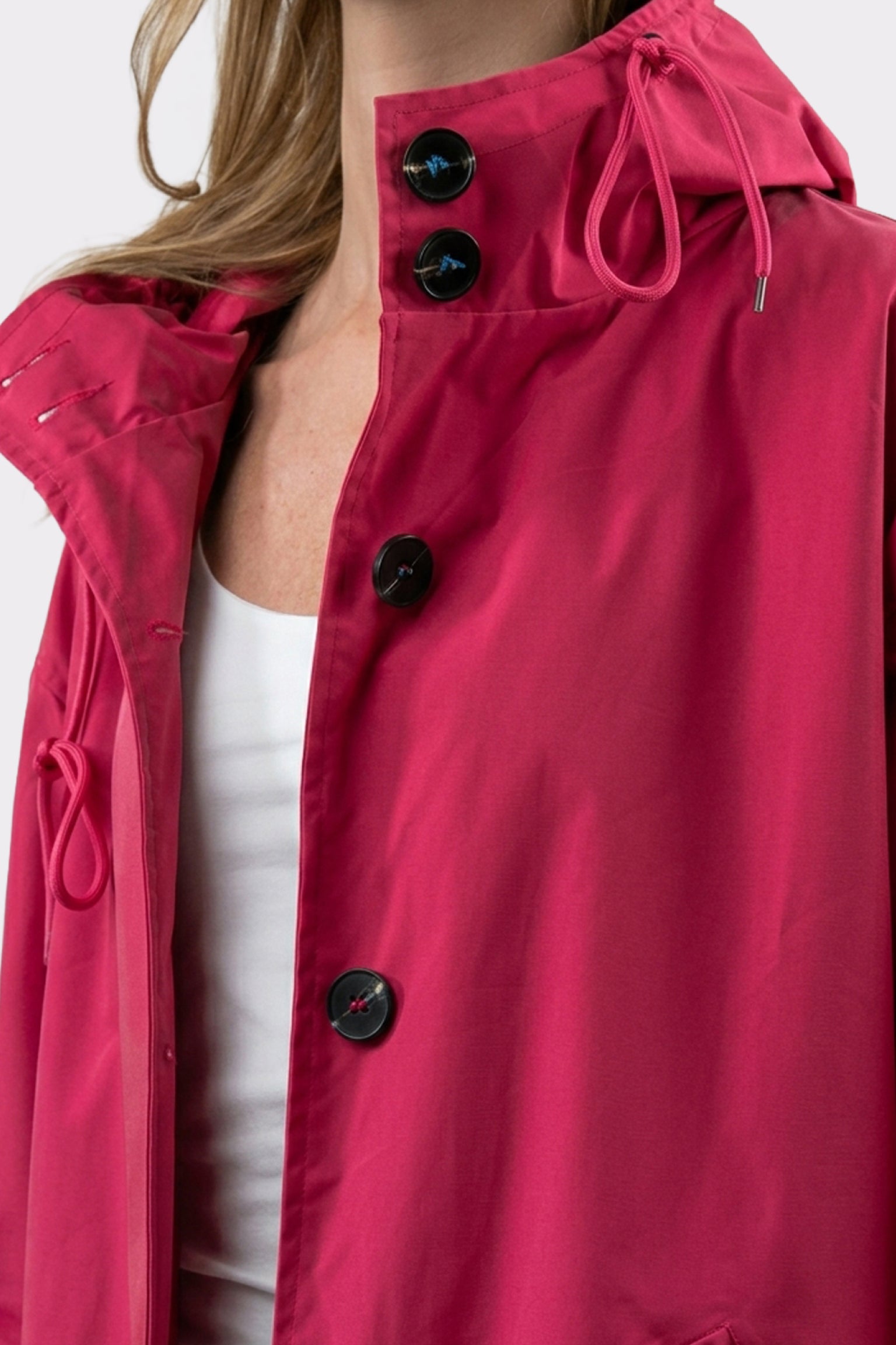 A person wearing The Water Resistant Hooded Oversized Windbreaker Rain Jacket in bright pink over a white top. The image is cropped to show only the upper torso and lower part of the face.