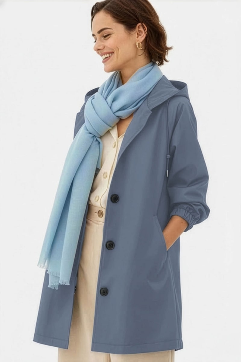 A woman faces left, smiling with her right hand in the pocket of a blue buttoned coat. She wears a cream outfit underneath and a looselyboho Sky Mist 100% Cashmere Scarf draped around her neck.