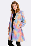 A person wears the looselyboho CANVAS SKY WINDBREAKER, a pastel tie-dye hooded jacket with black buttons and pockets, standing forward and slightly angled against a plain light background.