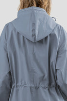 A person with light brown hair is seen from behind wearing The Windbreaker Jacket's POWDER BLUE WINDBREAKER. The water-resistant jacket features a loose fit with a cinched detail at the waist, set against a plain gray background.