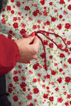 Wearing a red sleeve, someone ties a red string on a looselyboho BURGUNDY BLOSSOM WINDBREAKER featuring water-resistant fabric with a white background and red floral pattern.