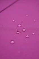 Close-up of water droplets on smooth pink fabric highlights the water-repellent design of the looselyboho Water-Repellent Rain & Shine A-Line Hooded Raincoat—a stylish women’s coat for staying dry in any weather.