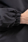 Close-up of an arm wearing a stylish **looselyboho ONYX BLACK WINDBREAKER** with an elasticated cuff, showing part of the wrist and hand.